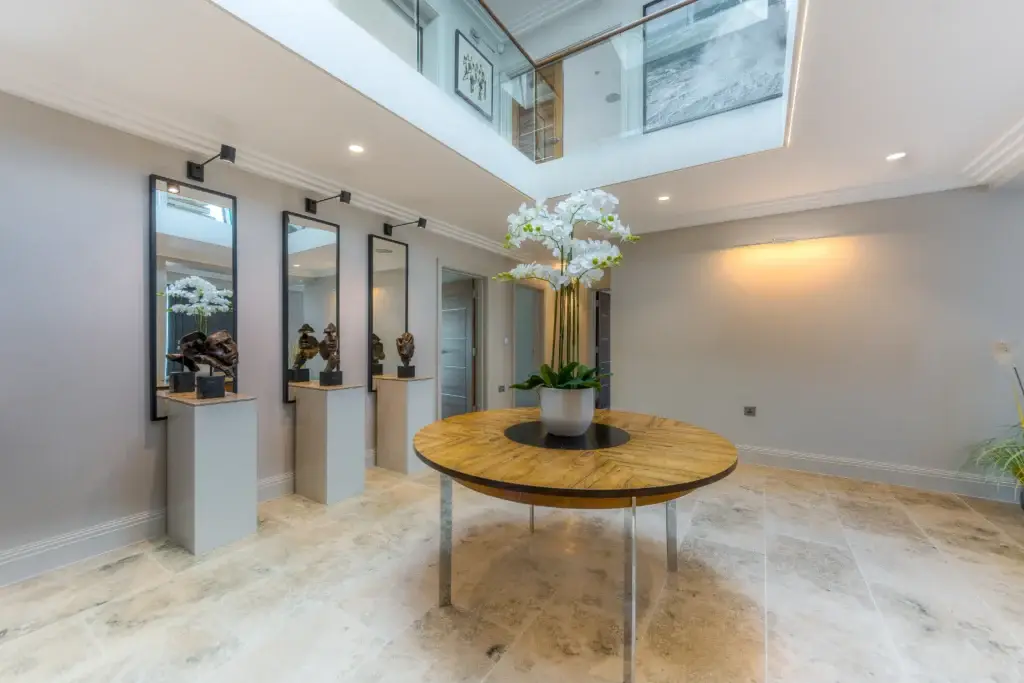 Bespoke round hallway table beneath rooflight, surrounded by sculptural art and marble-effect flooring in a handmade Worthing interior.