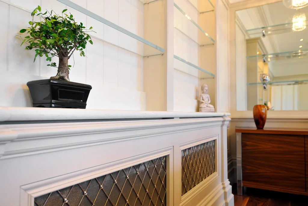 Custom white built-in shelving with glass shelves, bonsai tree, and decorative radiator cover in a bespoke Worthing interior