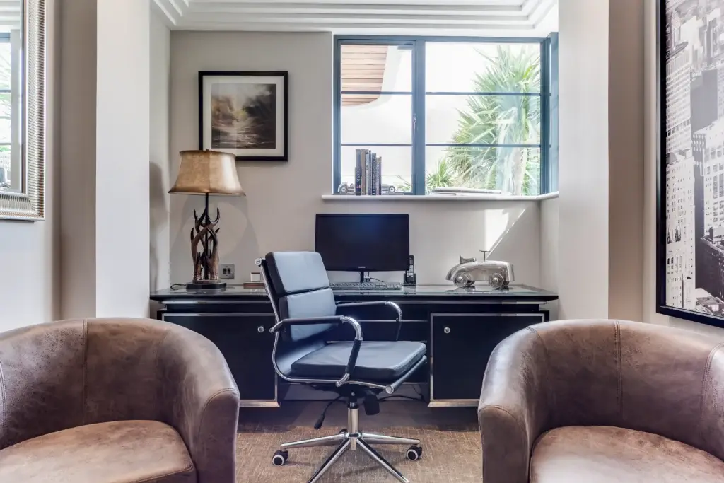 Bespoke home office in Worthing featuring a handmade desk, leather armchairs, and natural light through casement windows.